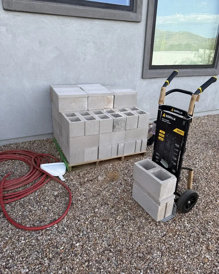 Side yard with leftover cinder blocks, a hose, and a hand truck.